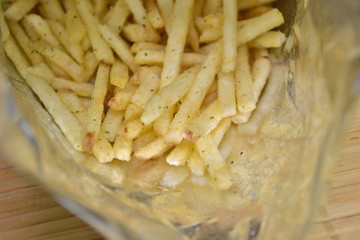 Snack french fries in foil pack. Fried potatoes inside the packaging on a wooden mat closeup