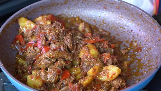 Frying pan with onion, lemongrass, red pepper and beef meat, close up. Indonesia. Sambal Goreng Ati Kentang, Indonesian cuisine, spicy beef meet and potatoes garnish with lemongrass leaf and red chili