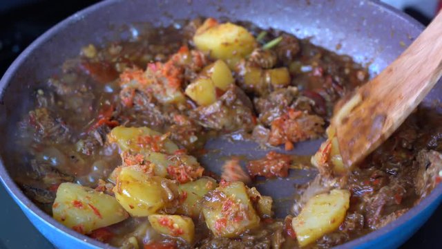 Frying pan with onion, lemongrass, red pepper and beef meat, close up. Indonesia. Sambal Goreng Ati Kentang, Indonesian cuisine, spicy beef meet and potatoes garnish with lemongrass leaf and red chili