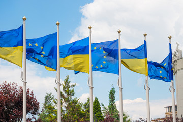 Row of flagpoles with European Union and Ukraine flags fluttering by wind on blue sky background