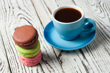 Full ceramic cup of hot black coffee near scattered sweet macaroons on old weathered rustic white table