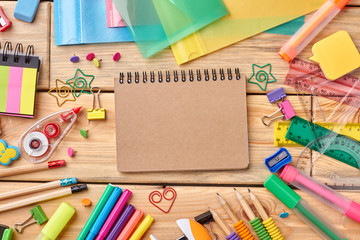 Notebook and school accessories on wooden background. School supplies on wooden table, top view.