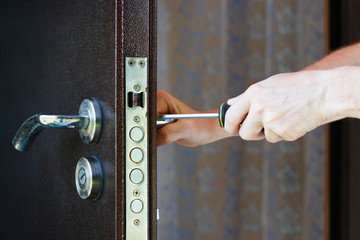 Handyman repair the door lock in metal entrance door, man fixing lock with screwdriver, closeup of repairing door.