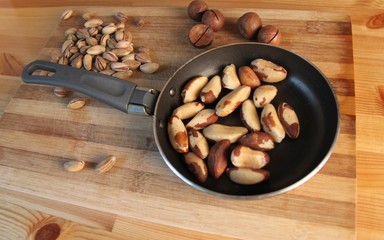 Brazil nuts, pistachios, macadamia scattered on a small pan and a wooden Board, which stands on a wooden Board striped texture, close-up.