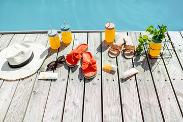 View on the poolside with accessories for summer vacations, drinks, slippers, sunglasses, sunscreen lotions and hat