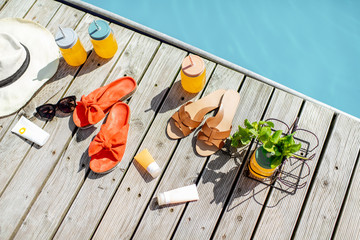 View on the poolside with accessories for summer vacations, drinks, slippers, sunglasses, sunscreen lotions and hat