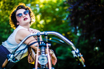 Obraz na płótnie Canvas A pinup woman in a vintage dress posed next to the old motorcycle
