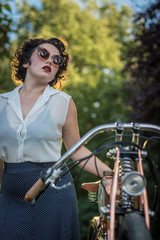 Fototapeta na wymiar A pinup woman in a vintage dress posed next to the old motorcycle