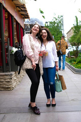 Two young girls walking, laughing and chatting. Girlfriend walking on the street along the summer cafe. In the hands of cold drinks