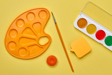Art supplies on yellow background. Watercolor palettes, paintbrush and sticky note on color background. Education and creativity concept.