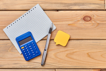 Office supplies on wooden background. Sticky note, calculator, notebook, ballpoint pen. Business and work concept.