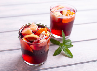 Two glasses with sangria next to mint leaves, on wooden table. Typical Spanish drink with wine and fruits.