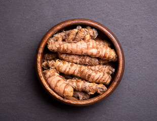 Turmeric roots in a wooden bowl on black slate table. Spice for health and cooking ingredient.