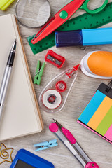 School accessories background, top view. Notebook and various office supplies on grey wooden surface.