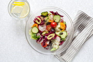 Green vegan salad from green leaves mix and vegetables. Top view on white stone table.