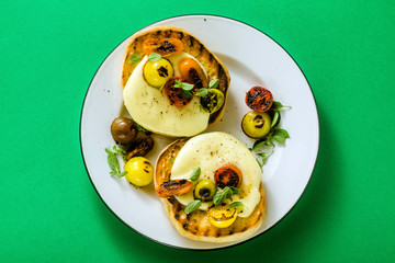 melted cheese sandwich on grilled bread with caramelized multi-colored cherry tomatoes and fresh sage on a green background
