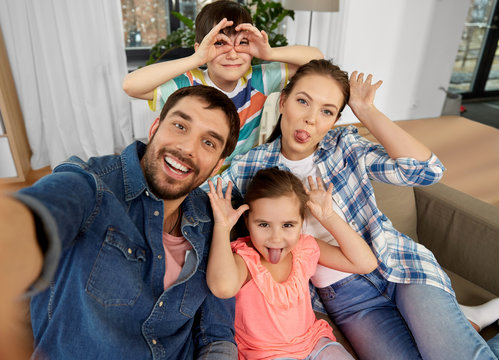 family, fun and people concept - happy father, mother, little son and daughter taking selfie and making faces at home