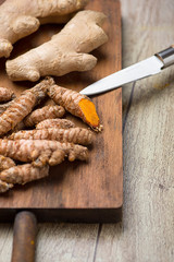 Vertical shoot of turmeric roots next to knife and spoon on cutting board in the kitchen. Specia for health and cooking ingredient.