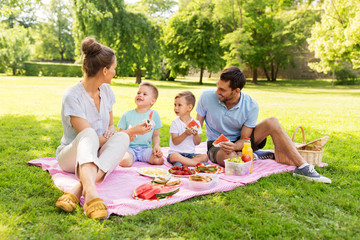 family, leisure and people concept - happy mother, father and two little sons having picnic and eating watermelon at summer park - obrazy, fototapety, plakaty