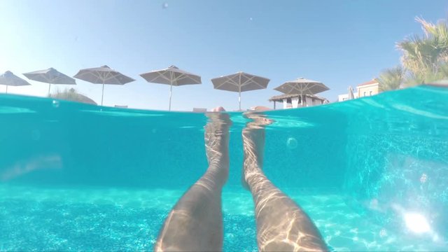 View of male's legs floating under the crystal clear blue water in cute modern and clean swimming pool on hot sunny day, view from inside of pool.