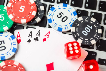 Online poker casino theme. Gambling chips with dice and aces playing cards on laptop.