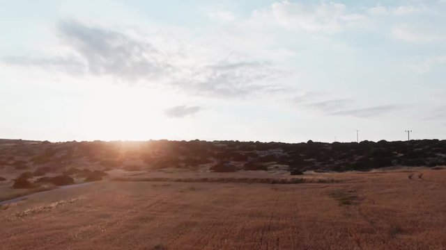 Beautiful rocky hills and wheat field in the countryside. Drone view of the rural farmland, road and hills on the island under sunset in summer.