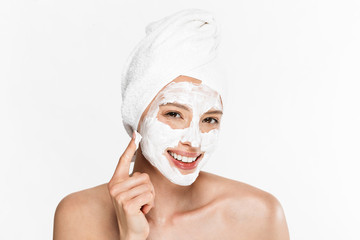 Image of gorgeous half-naked woman wrapped in towel applying facial cream and smiling at camera