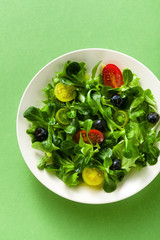fresh salad of arugula and valerian leaves with colored tomatoes and blueberries in a plate on a green background.