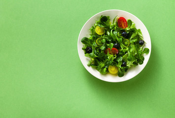 fresh salad of arugula and valerian leaves with colored tomatoes and blueberries in a plate on a green background.