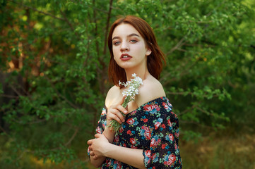 Open portrait of a young beautiful girl in a summer dress , model holding flowers