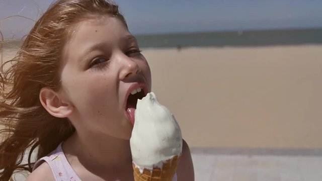 jolie fillette d&eacute;gustant une cr&egrave;me glac&eacute;e sur la plage ensoleill&eacute;e