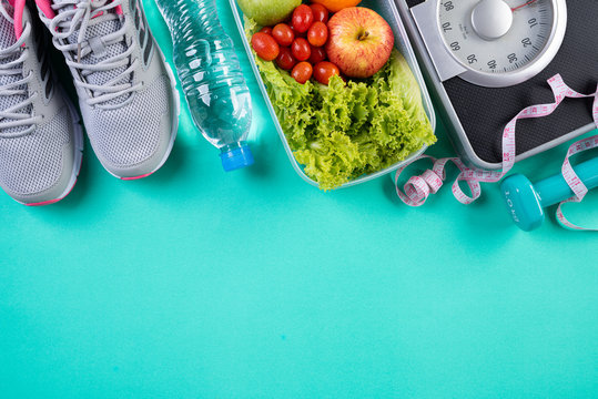 Healthy lifestyle, food and sport concept. Top view of athlete's equipment Weight Scale measuring tape blue dumbbell, sport water bottles, fruit and vegetables on green pastel background. © Siam