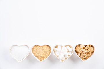 Top view of various types of sugar. Cube sugar, raw sugar brown sugar and granulated sugar in heart bowl on white background. Flat lay.