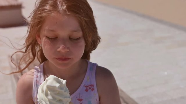 jolie fillette d&eacute;gustant une cr&egrave;me glac&eacute;e sur la plage ensoleill&eacute;e