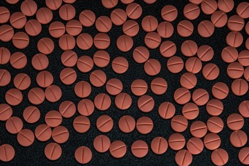 Orange colour round pills on black background with selective focus. Pills that look like ecstasy.