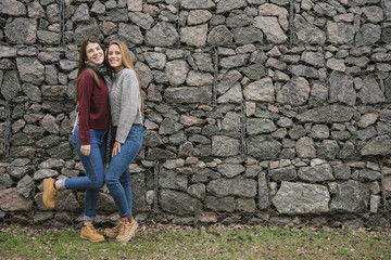 Obraz na płótnie Canvas Two smiling young women in front of stone wall