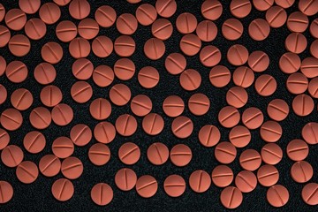 Orange colour round pills on black background with selective focus. Pills that look like ecstasy.