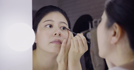 Asian woman actress getting ready applying black eyeliner eye pencil on eyes looking in mirror of vanity table. reflection of gorgeous lady performer doing makeup in dressing place in backstage.