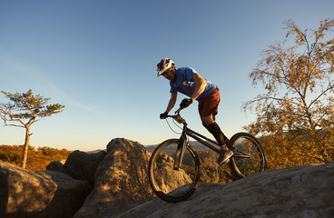 Athletic male cyclist riding on trial bicycle on top of mountain, rider making acrobatic trick on...