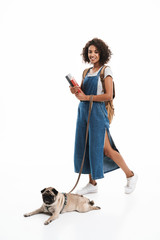 Image of pleased african american woman wearing backpack holding books and poising with her pug