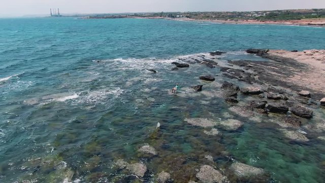 Aerial shot of the beautiful seaside on a rocky island. Drone view of the funny man king of the ocean sitting on the water on the seashore.