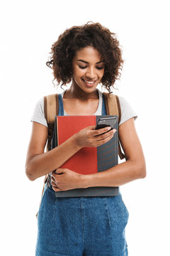 Image of young african american woman wearing backpack holding exercise books and cellphone