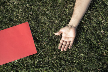 hand and red book on grass