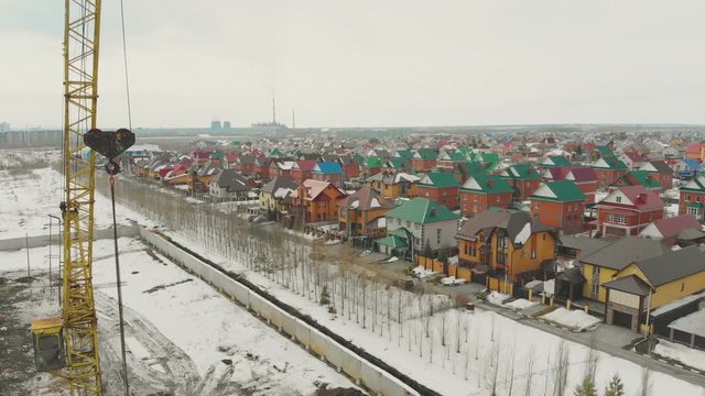 yellow tower crane with hook on construction site near comfortable cottages on nasty frosty day aerial view