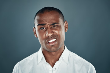 Feeling uncertain. Young African man in shirt looking at camera and frowning while standing against grey background