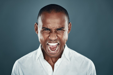 Obraz premium So angry! Displeased young African man in shirt looking at camera and shouting while standing against grey background