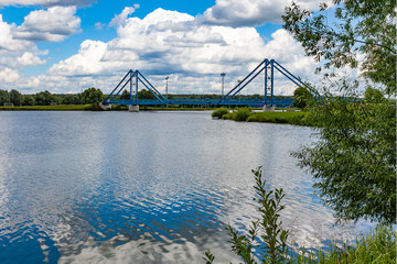 Scenic metal pedestrian bridge across the river against a cloudy sky