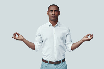 Fototapeta premium Find your balance. Handsome young African man meditating while standing against grey background