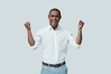 Fototapeta premium Cheering. Handsome young African man gesturing and smiling while standing against grey background