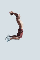 On the way to success. Full length of young African man in sport clothing making a face while jumping against grey background